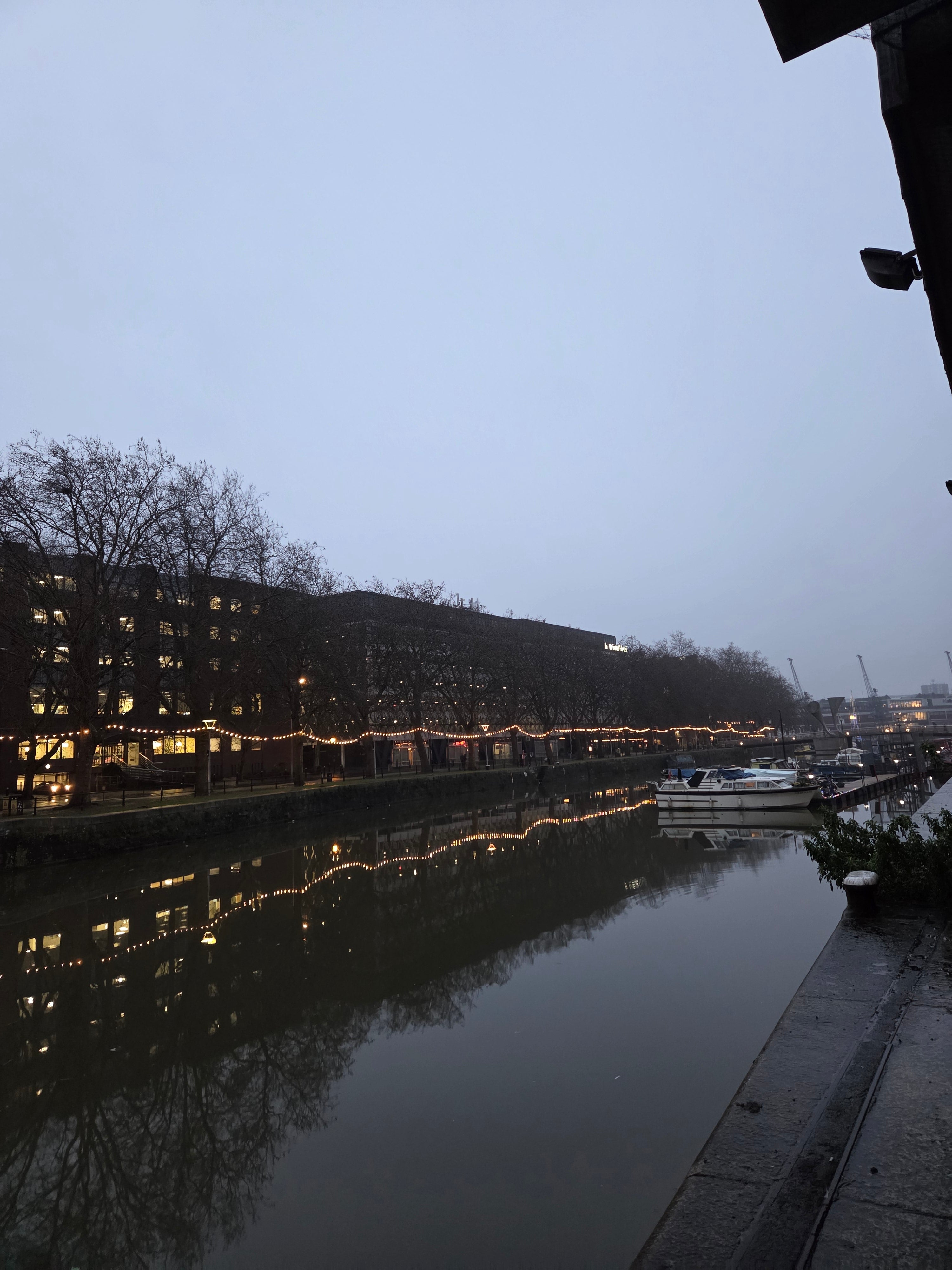 Tall building with lights at night, reflected in water in Bristol Harborside
