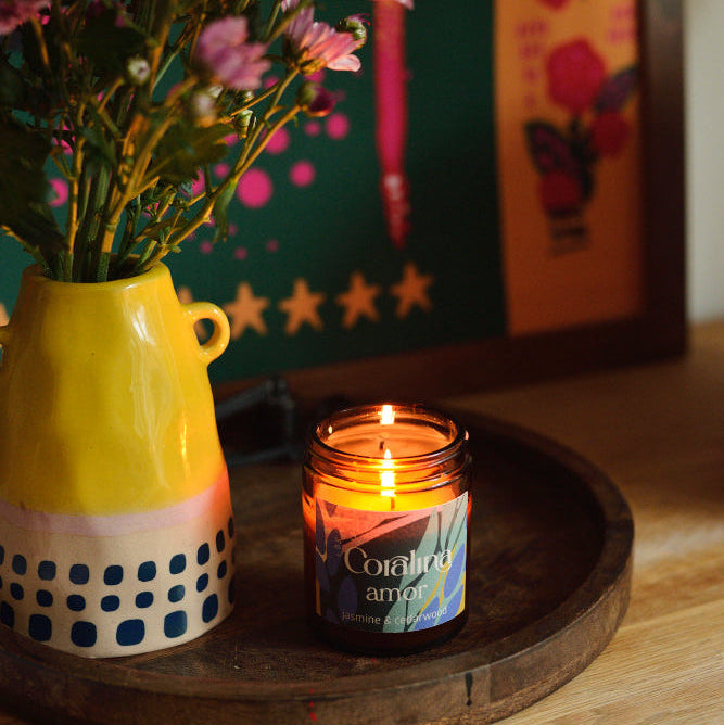 Candle in a jar with flowers in a yellow vase on a wooden surface