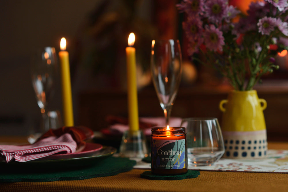 Candlelit table setting with wine glasses, flowers, and a vase.