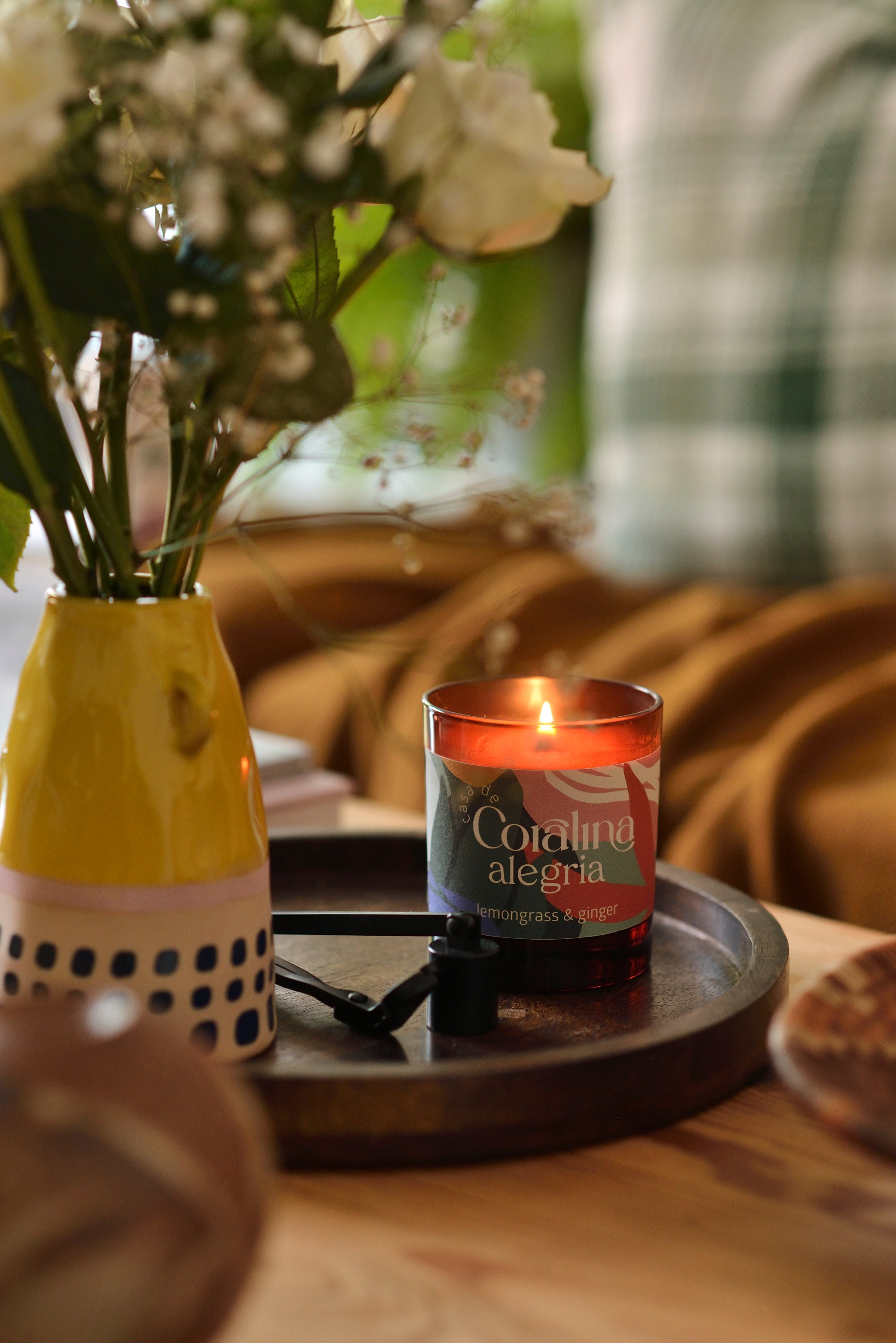 Candle labeled 'Coraling alegría' on a wooden tray with flowers in the background